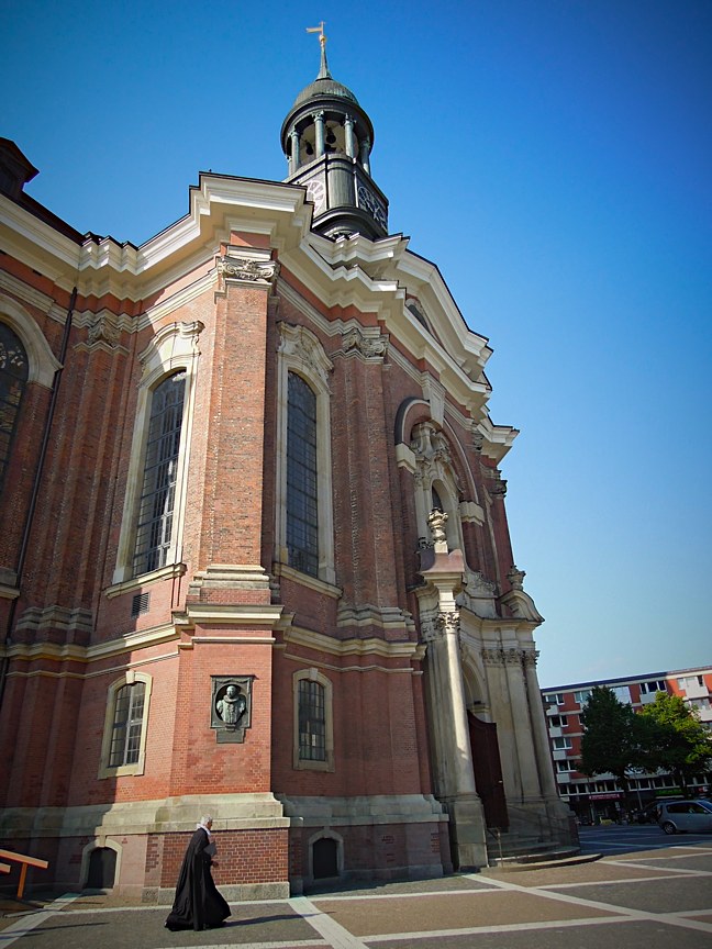 Fassade des Michels mit Turm im Hintergrund und Pfarrer im Vordergrund